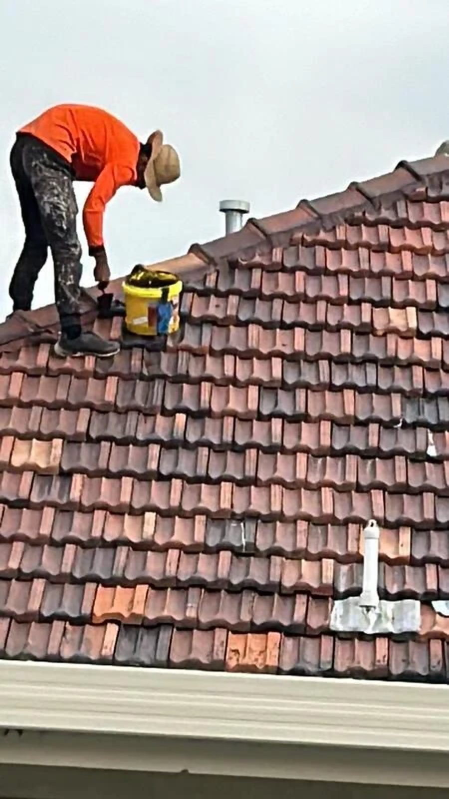 Roofer repointing ridge caps on a terracotta tile roof